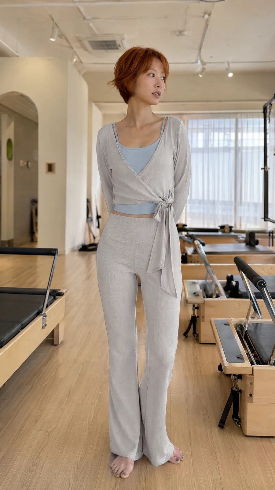 グレーのリブ編みラップセットを着た女性がピラティススタジオに立っている
